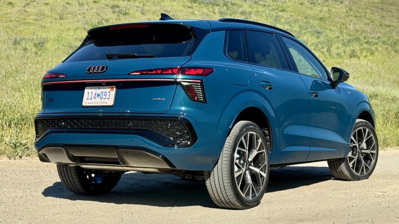 A rear three-quarters shot of the blue Q3 parked on dirt in front of a grassy hill A rear three-quarters shot of the blue Q3 parked on dirt in front of a grassy hill