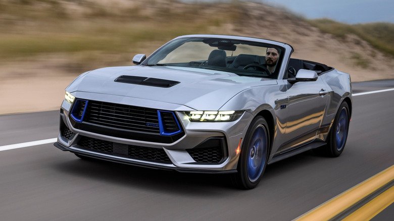 A silver and blue Ford Mustang California Special driving on a road.