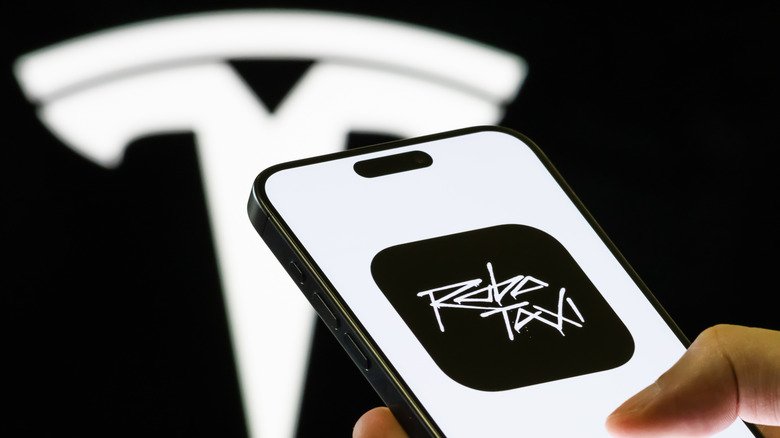 In this photo illustration, a smartphone held in a hand shows the [Tesla Robotaxi](/article/tesla-semi-2026-production-de-masse-specs-et-165-m-de-subventions) app, a platform allowing users to join the waitlist for autonomous ride-hailing services using [Tesla Model Y](/article/tesla-model-y-7-places-prix-autonomie-et-disponibilite-en-france) vehicles, with the company's branding seen in the background on September 4, 2025 in Chongqing, China.